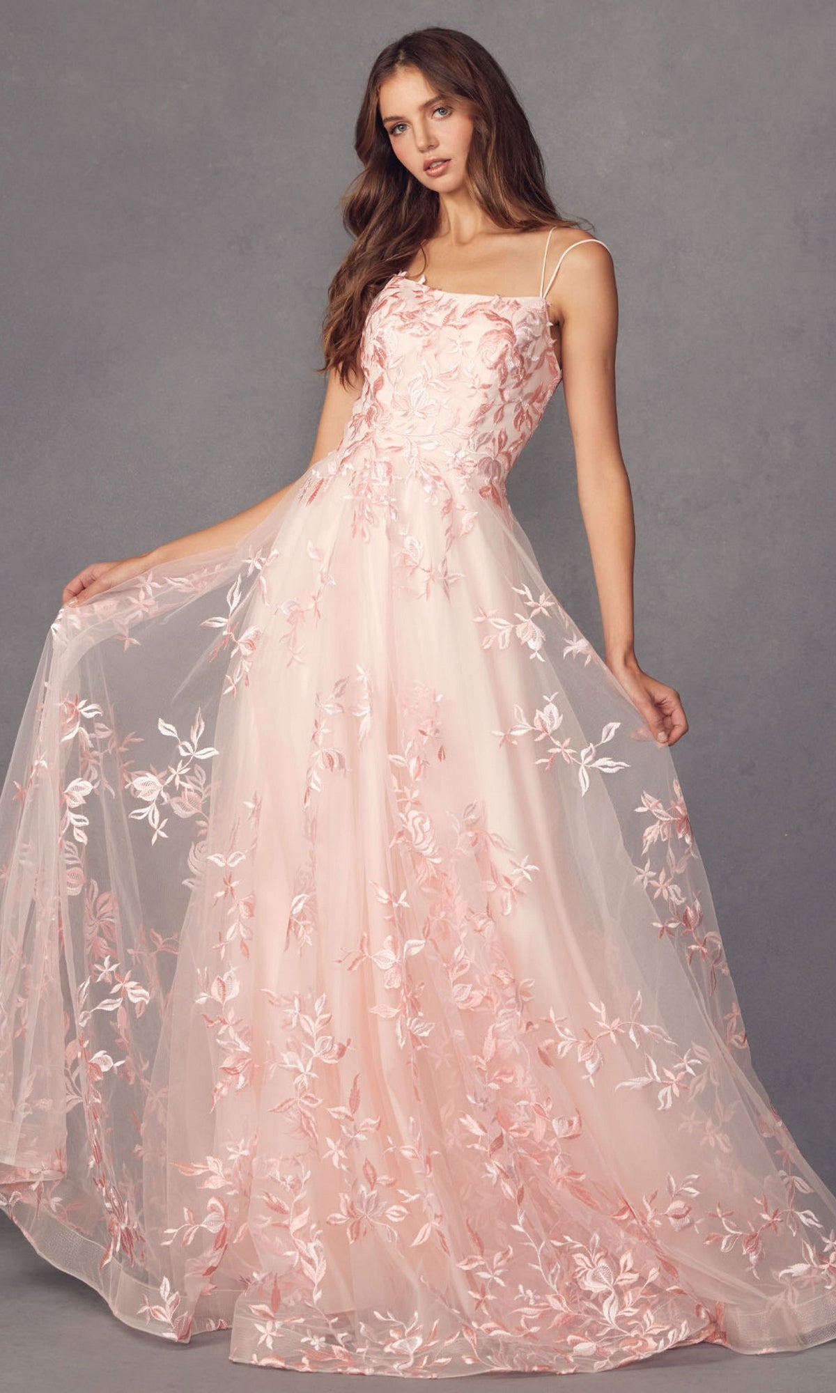 A woman models the Embroidered-Lace Long A-Line Prom Ball Gown 279, a floor-length light pink dress with floral embroidery and thin straps, holding out the skirt against a plain gray background.